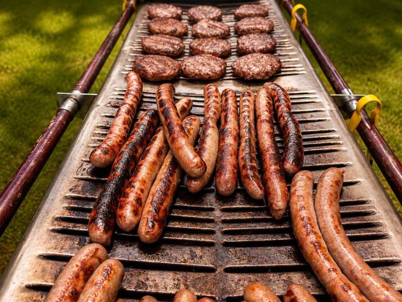 Sausages and burgers sizzling on a large outdoor grill