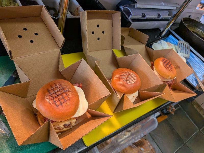 Three toasted brioche burgers with egg and bacon in open takeaway boxes