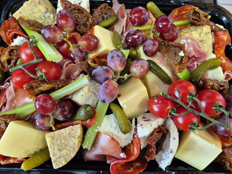 A platter of cheeses, cured meats, grapes, vine tomatoes, celery and gherkins