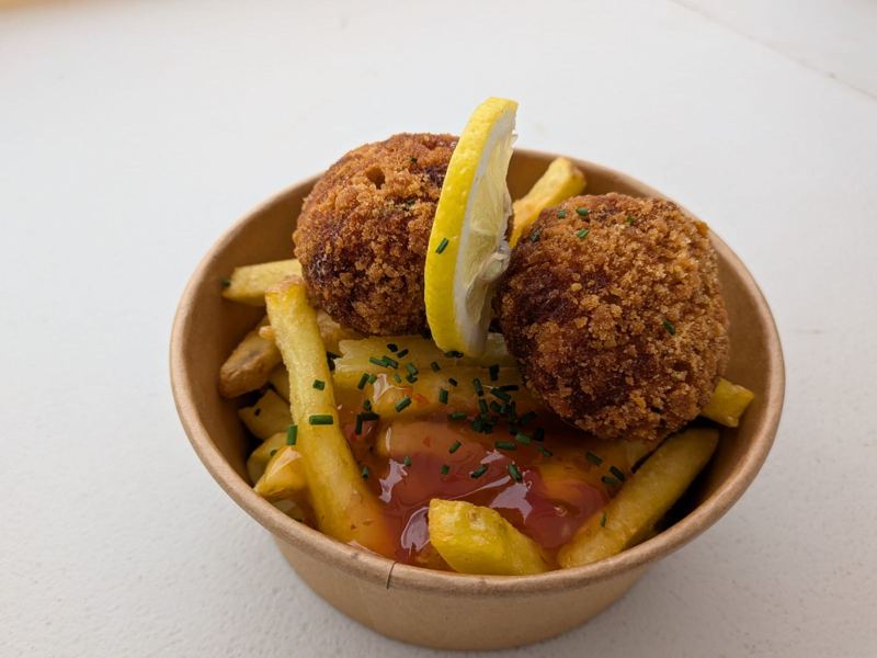 Two crab cakes on chips with sweet chilli sauce and a slice of lemon