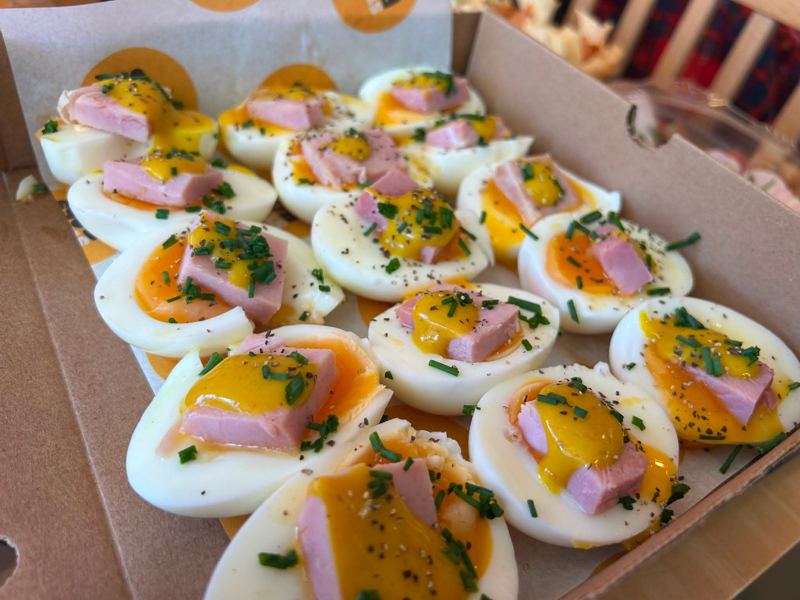 Halved soft-boiled eggs topped with ham, mustard sauce and chives