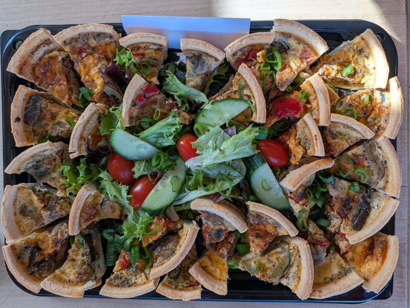 A tray of quiche slices arranged around a mixed salad with cherry tomatoes