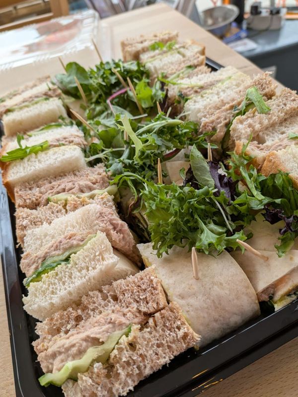 A platter of white and brown sandwiches and wraps with salad leaves