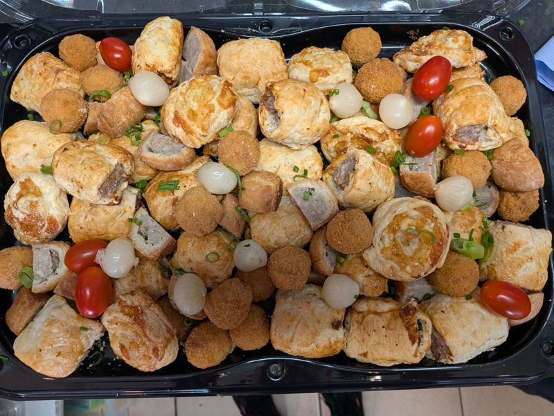 A tray of sausage rolls and scotch egg bites with pickled onions and cherry tomatoes