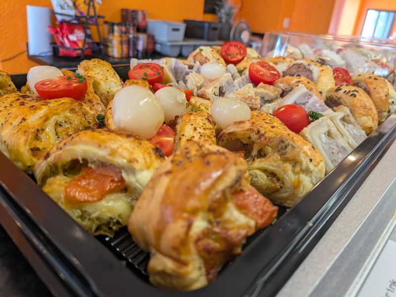 A tray of golden savoury pastries and pork pie with pickled onions and cherry tomatoes