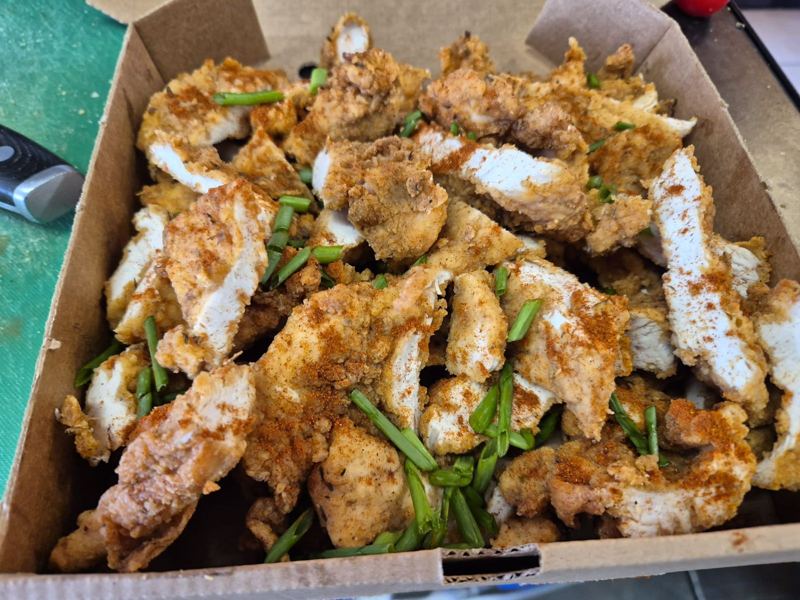 A box of crispy seasoned chicken strips sprinkled with paprika and spring onion