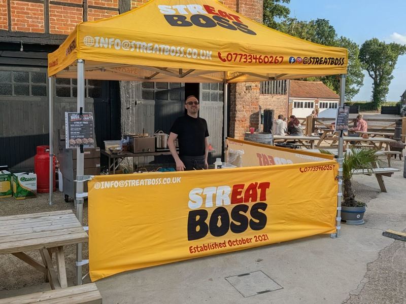 A Streat Boss chef smiling behind the yellow branded gazebo stall in a pub courtyard